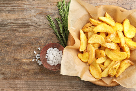 Bowl with tasty baked potato wedges on wooden background, top view. Space for textの写真素材