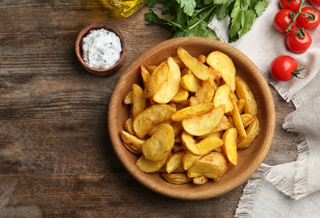 Bowl with tasty baked potato wedges on wooden background, top view. Space for textの写真素材