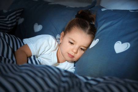 Beautiful little girl with gadget in bed at night. Bedtime scheduleの写真素材