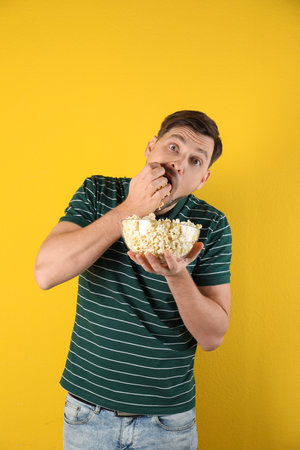 Man eating tasty popcorn on color backgroundの写真素材