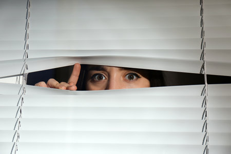 Curious woman looking through Venetian window blindsの写真素材