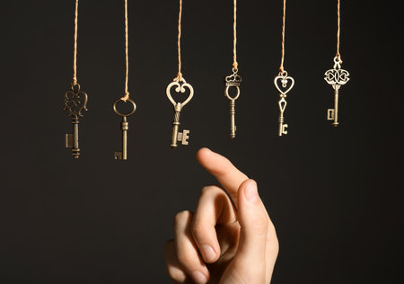Woman choosing among bronze vintage ornate keys hanging on threads against dark background, closeupの写真素材
