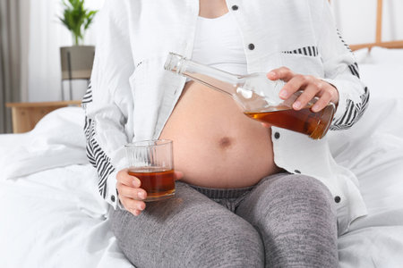 Pregnant woman pouring whiskey into glass at home. alcohol addictionの写真素材
