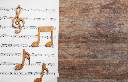 Music notes with sheet on wooden background, flat lay. Space for textの写真素材