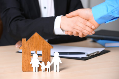 Man shaking hands with real estate agent at table, focus on family and house figures. home insuranceの写真素材