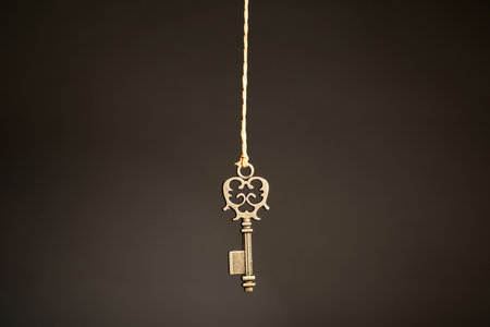 Bronze vintage ornate key hanging on thread against dark background