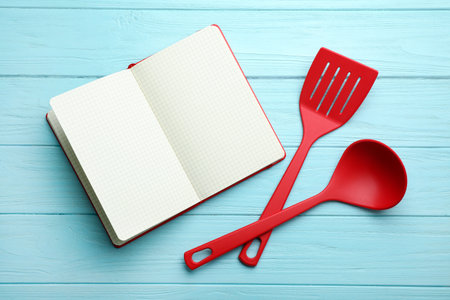 Soup ladle, spatula and empty recipe book on wooden background, top viewの写真素材