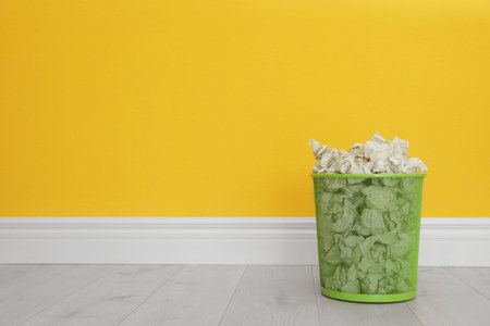 Metal bin with crumpled paper against color wall, space for textの写真素材