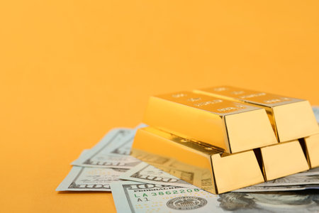 Shiny gold bars and dollar bills on color background. Space for textの写真素材