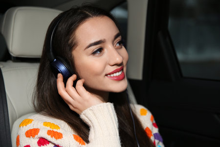 Beautiful young woman listening to music with headphones in car