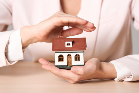 Female agent covering house model at table, closeup. home insuranceの写真素材