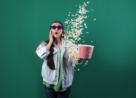 Emotional young woman with 3D glasses throwing popcorn on color backgroundの写真素材