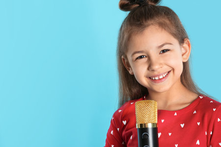 Cute funny girl with microphone on color background. Space for textの写真素材