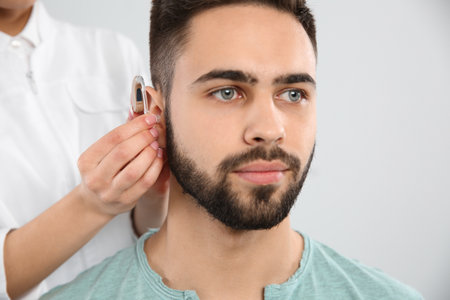 Otolaryngologist putting hearing aid in man's ear on white backgroundの写真素材