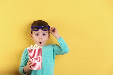 Cute little boy with popcorn and glasses on color background. Space for textの写真素材