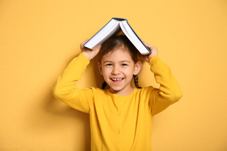 Cute little girl with book on color backgroundの写真素材