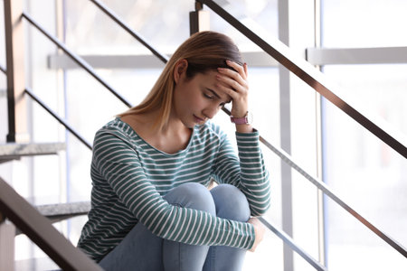Emotional teenage girl sitting on stairs indoorsの写真素材