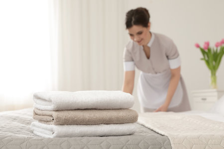 Young maid making bed in hotel room, focus on stack of towelsの写真素材