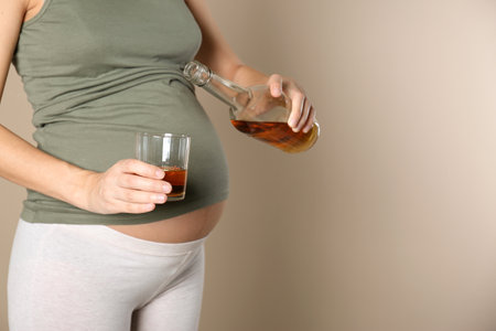 Pregnant woman pouring whiskey into glass on color background. alcohol addictionの写真素材