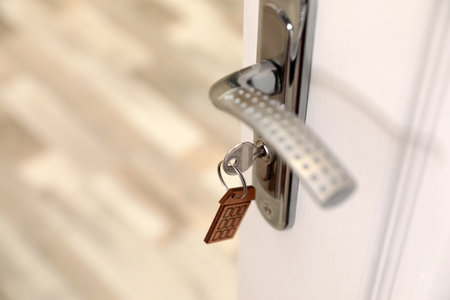 Key with house-shaped trinket in door lock, closeup. Space for text