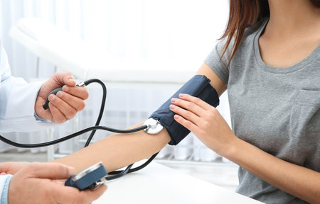 Young woman doctor visiting in hospital, closeup. Measuring blood pressure and checking pulse