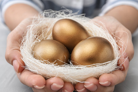 Woman holding nest with golden eggs over table, closeupの写真素材
