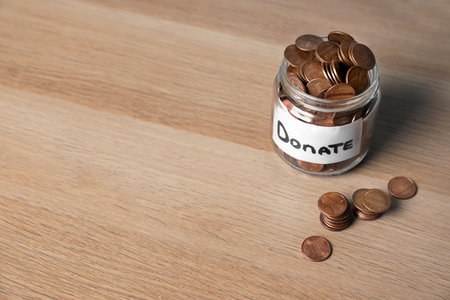 Glass jar with money and label DONATE on wooden background. Space for textの写真素材