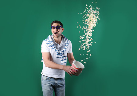 Emotional man with 3D glasses throwing popcorn on color backgroundの写真素材