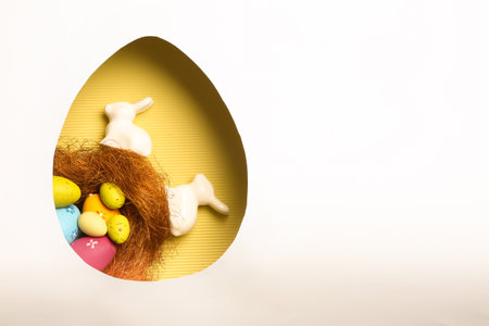 Top view of composition with Easter bunnies on color background through egg shaped hole, space for...