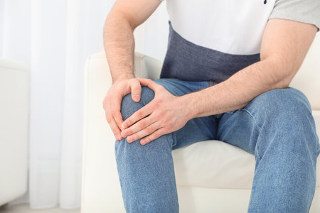Young man suffering from leg pain indoors, closeup. Space for textの写真素材