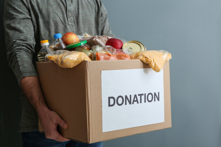 Man holding donation box with food on gray background, closeupの写真素材