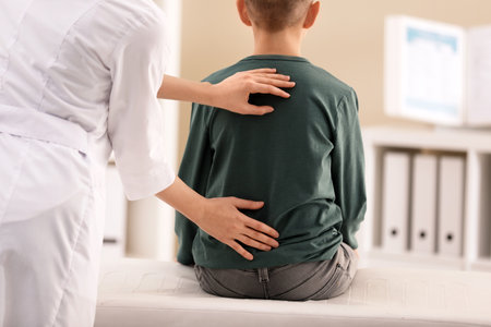 Chiropractor examining child with back pain in clinic, closeup