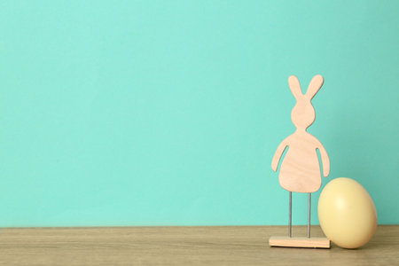 Cute wooden Easter bunny and dyed egg on table against color background, space for textの写真素材