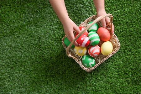 Little child with basket of painted Easter eggs on green grass, top view. Space for textの写真素材
