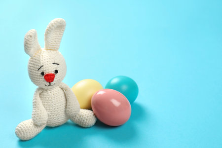 Cute Easter bunny toy and dyed eggs on color background, space for textの写真素材