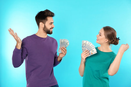 Happy young couple with money on color backgroundの写真素材