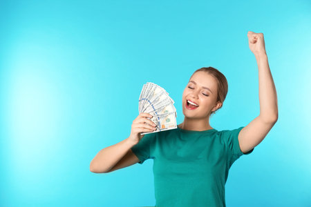 Portrait of happy young woman with money on color background. Space for textの写真素材
