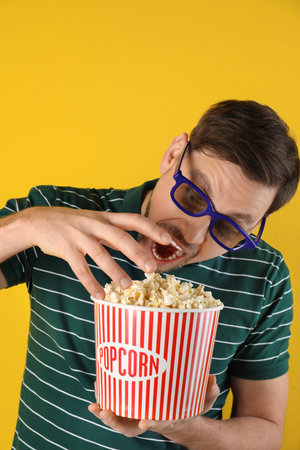 Man with 3D glasses eating tasty popcorn on color backgroundの写真素材