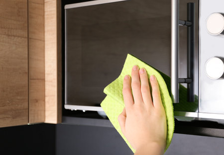 Woman cleaning microwave oven with rag in kitchen, closeupの写真素材
