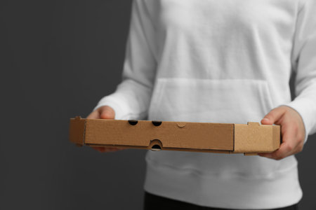 Young woman with pizza box on gray background, closeup. food delivery service