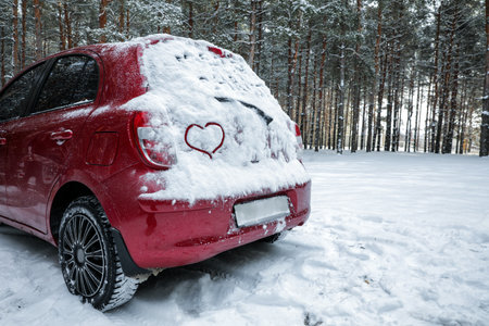 Heart drawing on snow covered car in winter forest. Space for textの写真素材