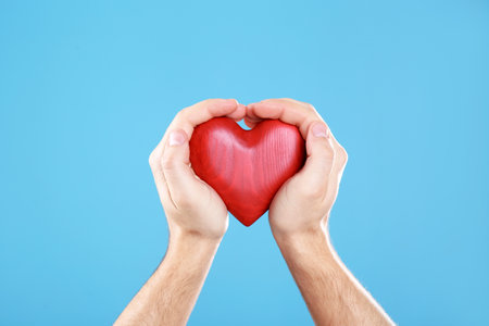 Man holding decorative heart in hands on color background, closeupの写真素材