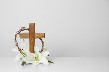 Wooden cross, crown of thorns and blossom lilies on table against light background, space for textの写真素材