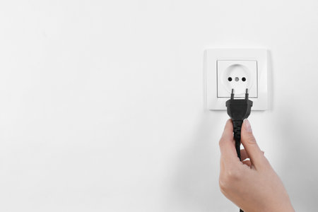 Woman putting plug into power socket on white background, closeup. Electrician's equipmentの写真素材