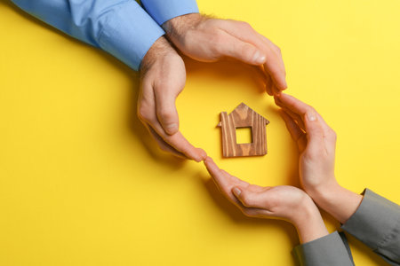 Couple holding hands near figure of house on color background, top view with space for text. home insuranceの写真素材