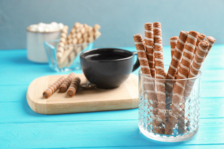 Glass with chocolate wafer rolls and cup of tea on wooden tableの写真素材
