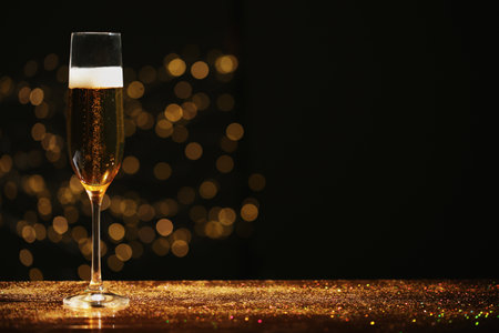 Glass of champagne and golden glitter on table against blurred background. Space for textの写真素材