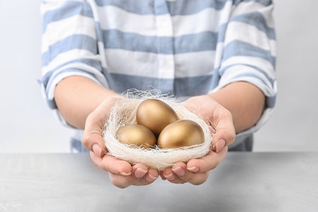 Woman holding nest with golden eggs over table on light background, closeupの写真素材