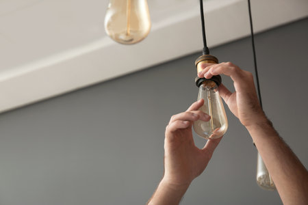Man changing lamp bulb indoors, closeup. Space for text