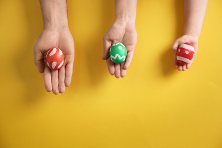 Father, mother and child holding painted Easter eggs on color background, top view. Space for textの写真素材